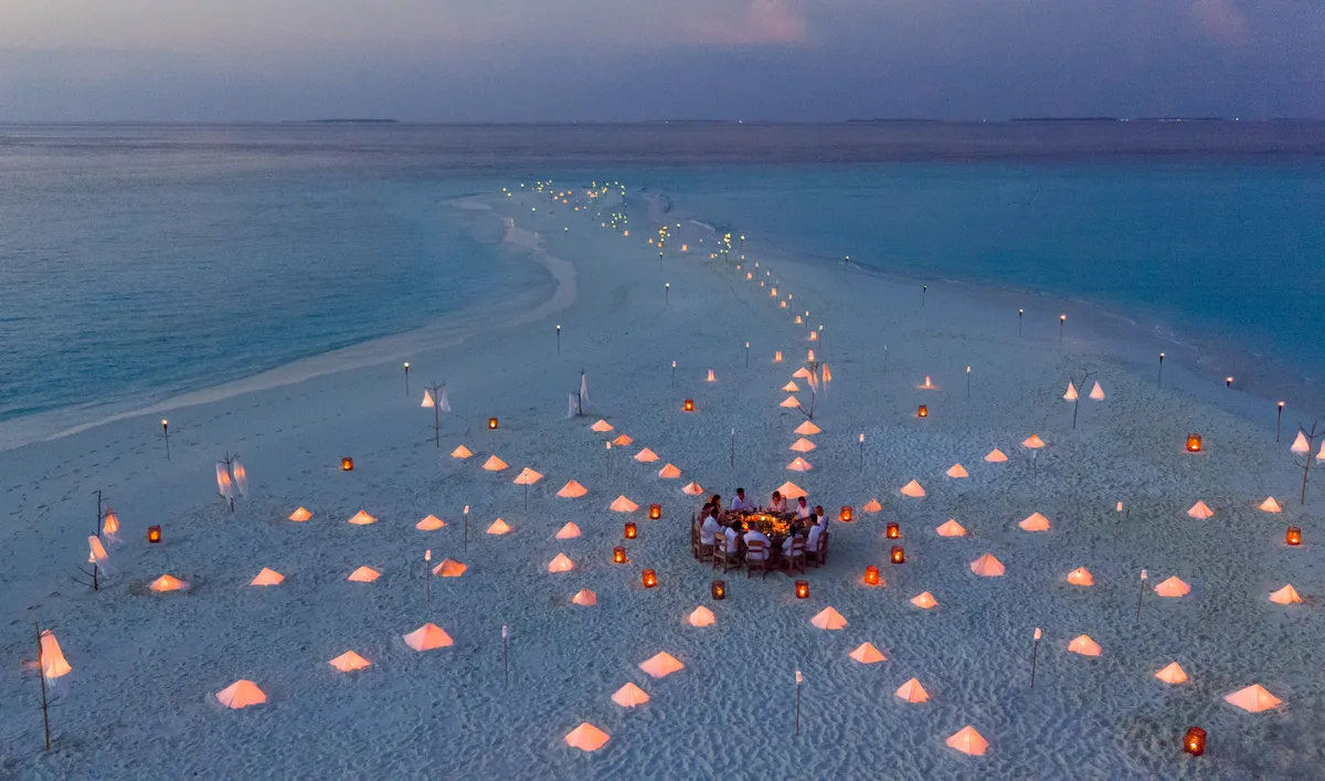 A private dinner table set alone on a sandbank at dusk