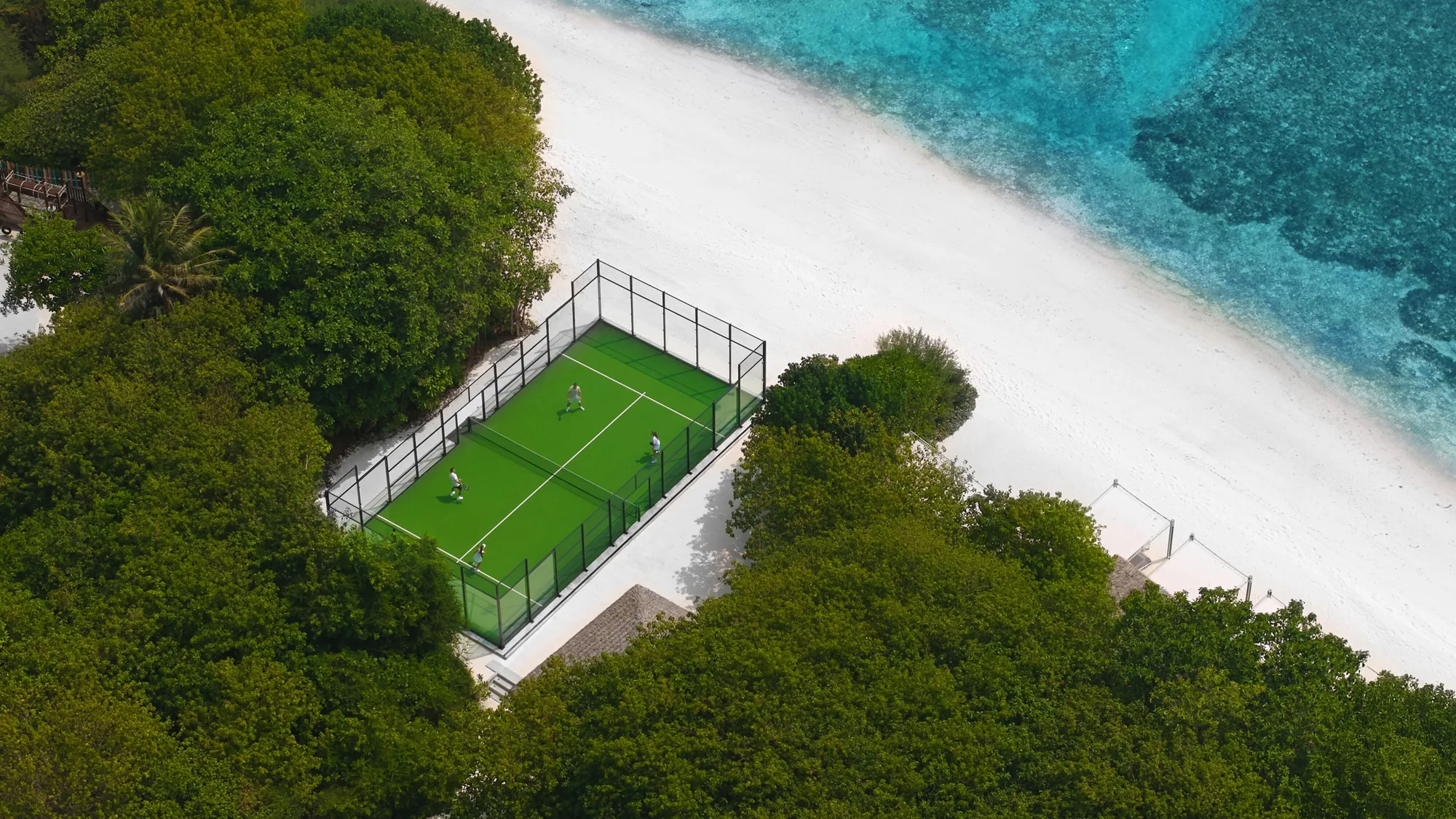 An aerial view of guests playing padel on a resort's beachfront court